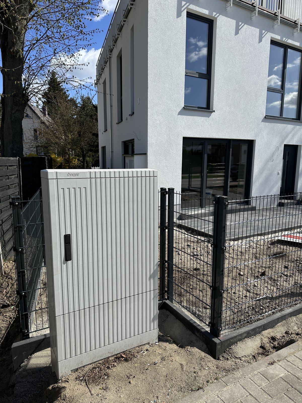 Grauer Zähleranschlussschrank auf Betonsockel an der Grundstücksgrenze eines neu gebauten Mehrfamilienhauses in Berlin