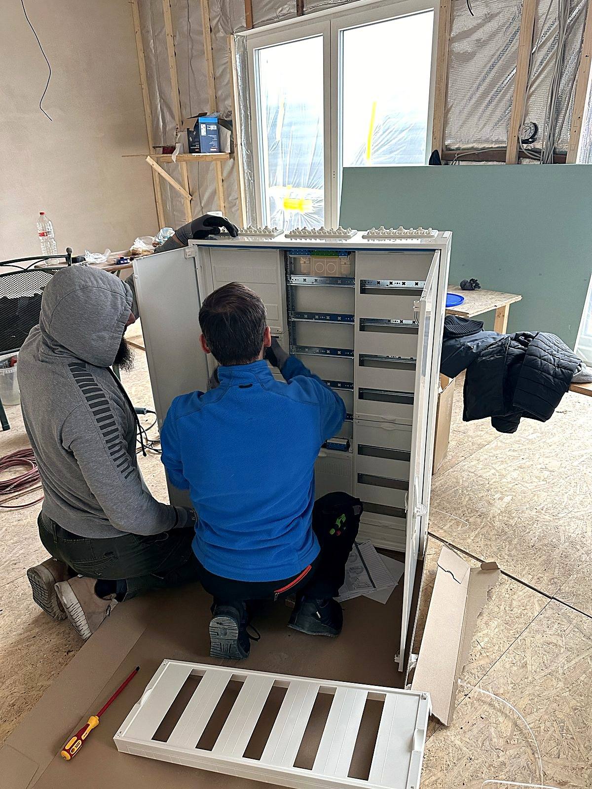 Zwei Elektriker beim Setzen und Verdrahten eines Zählerschranks auf einer Neubaubaustelle