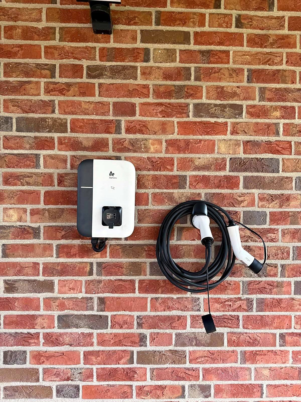 Weiße Wallbox mit aufgewickeltem Typ-2-Ladekabel an einer Klinkerfassade
