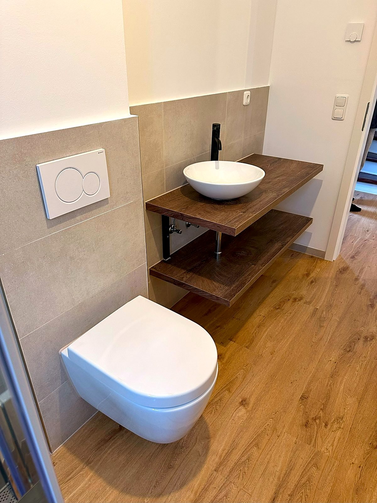 Fertiges Gäste-WC mit Wand-WC, Aufsatzwaschbecken auf Holzkonsole und großformatigen Fliesen