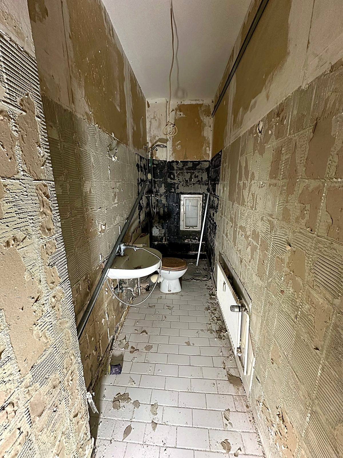 Altes Badezimmer im Rückbau mit abgeschlagenen Fliesen und freiliegenden Leitungen