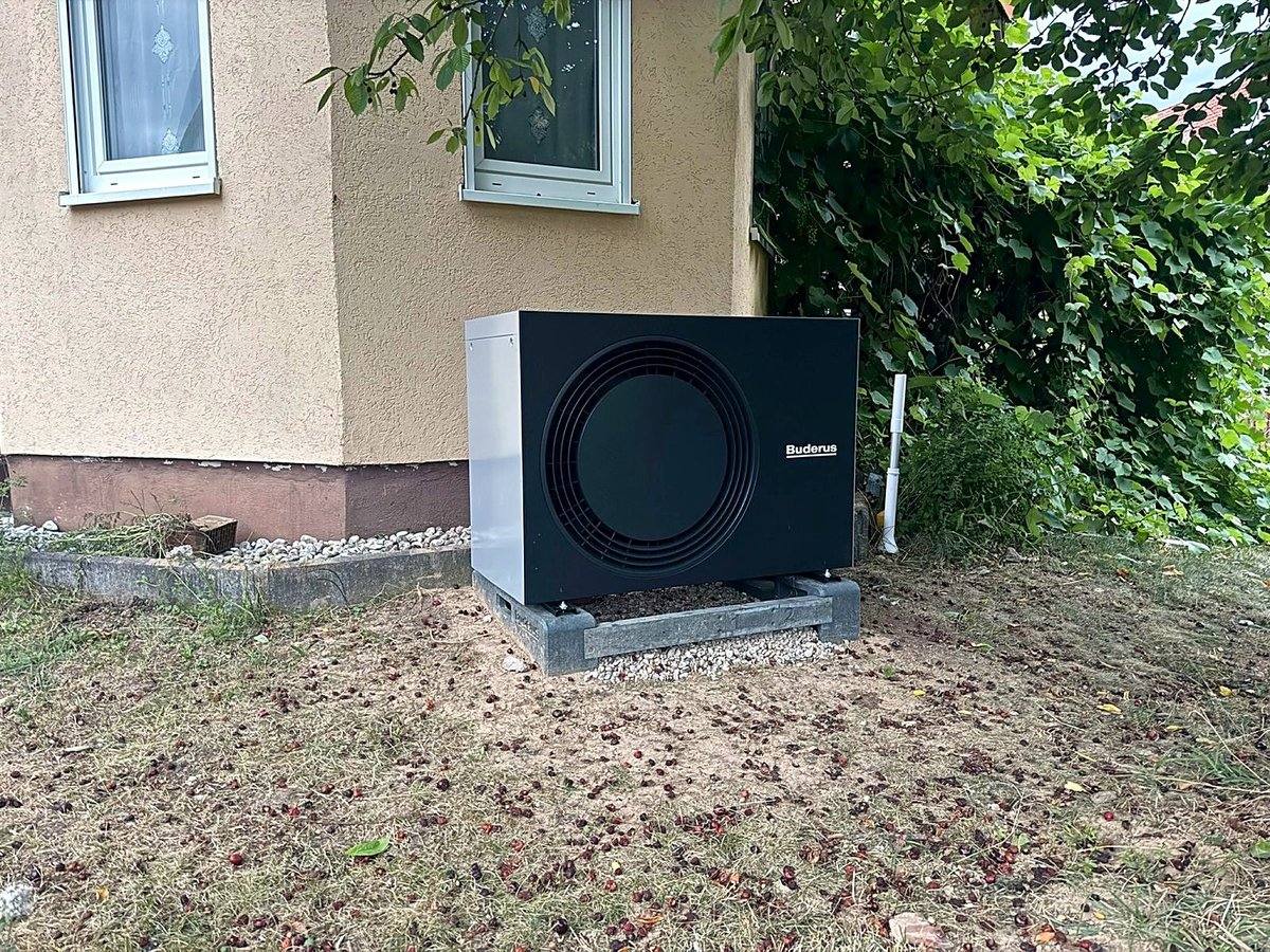 Buderus Wärmepumpen-Außengerät auf Betonauflagern neben einem Wohnhaus, aufgestellt auf der Rasenfläche
