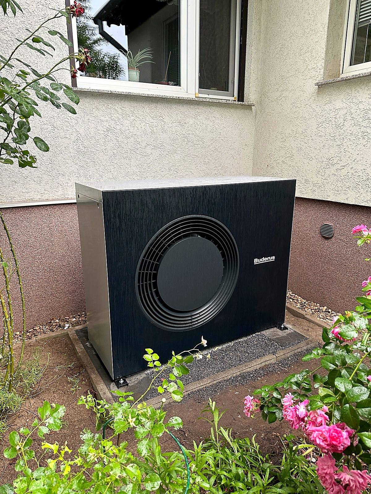 Schwarze Buderus Wärmepumpe an einer Hauswand neben einem Rosenbeet