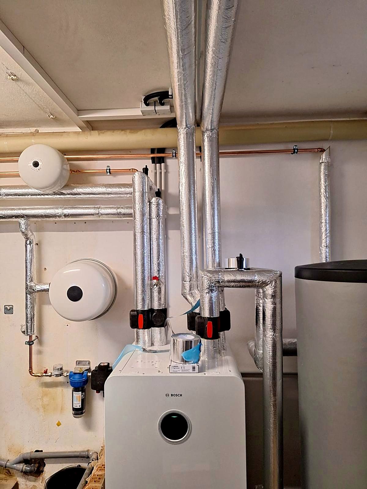 Bosch Wärmepumpen-Inneneinheit mit Pufferspeicher und gedämmten Leitungen im Heizungskeller