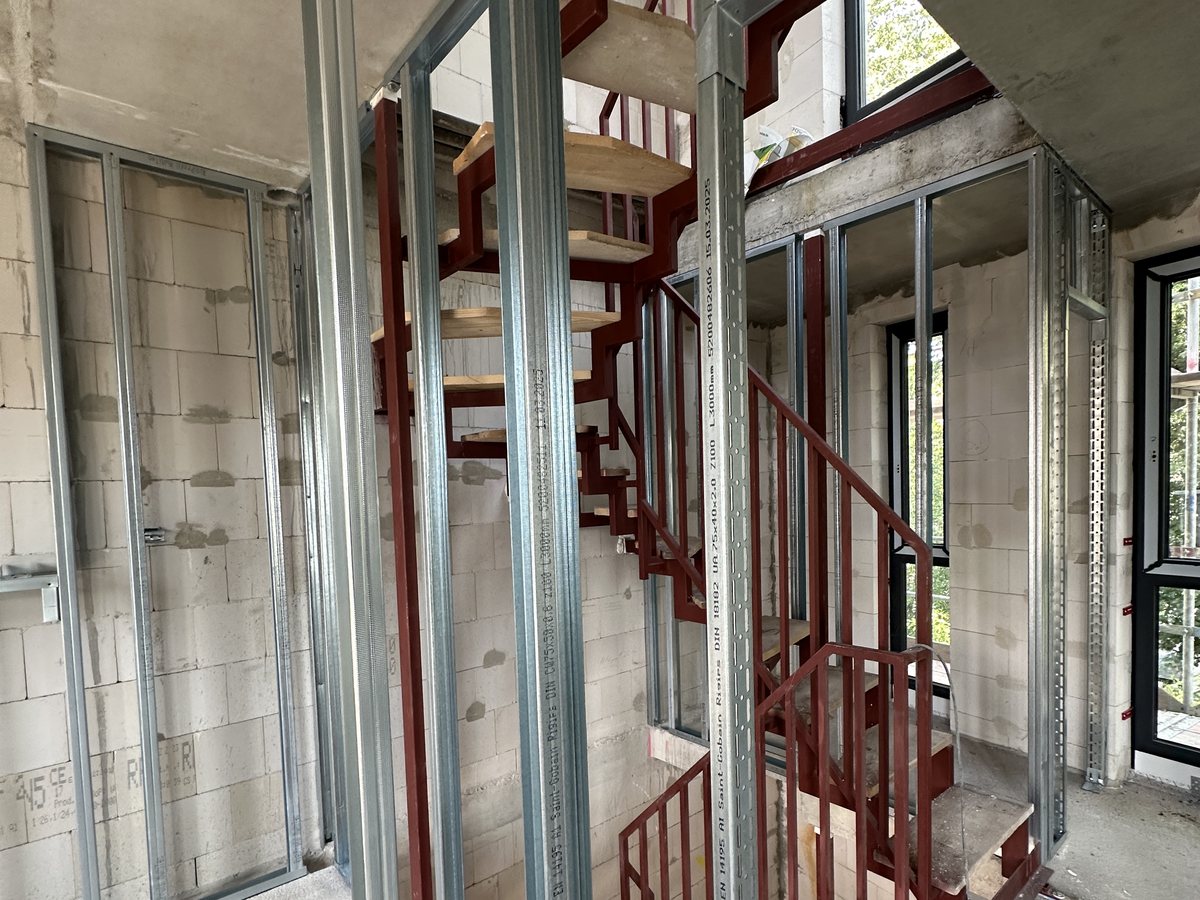 Rot grundierte Stahltreppe im Rohbau, davor Trockenbau-Ständerwerk aus CW-Profilen