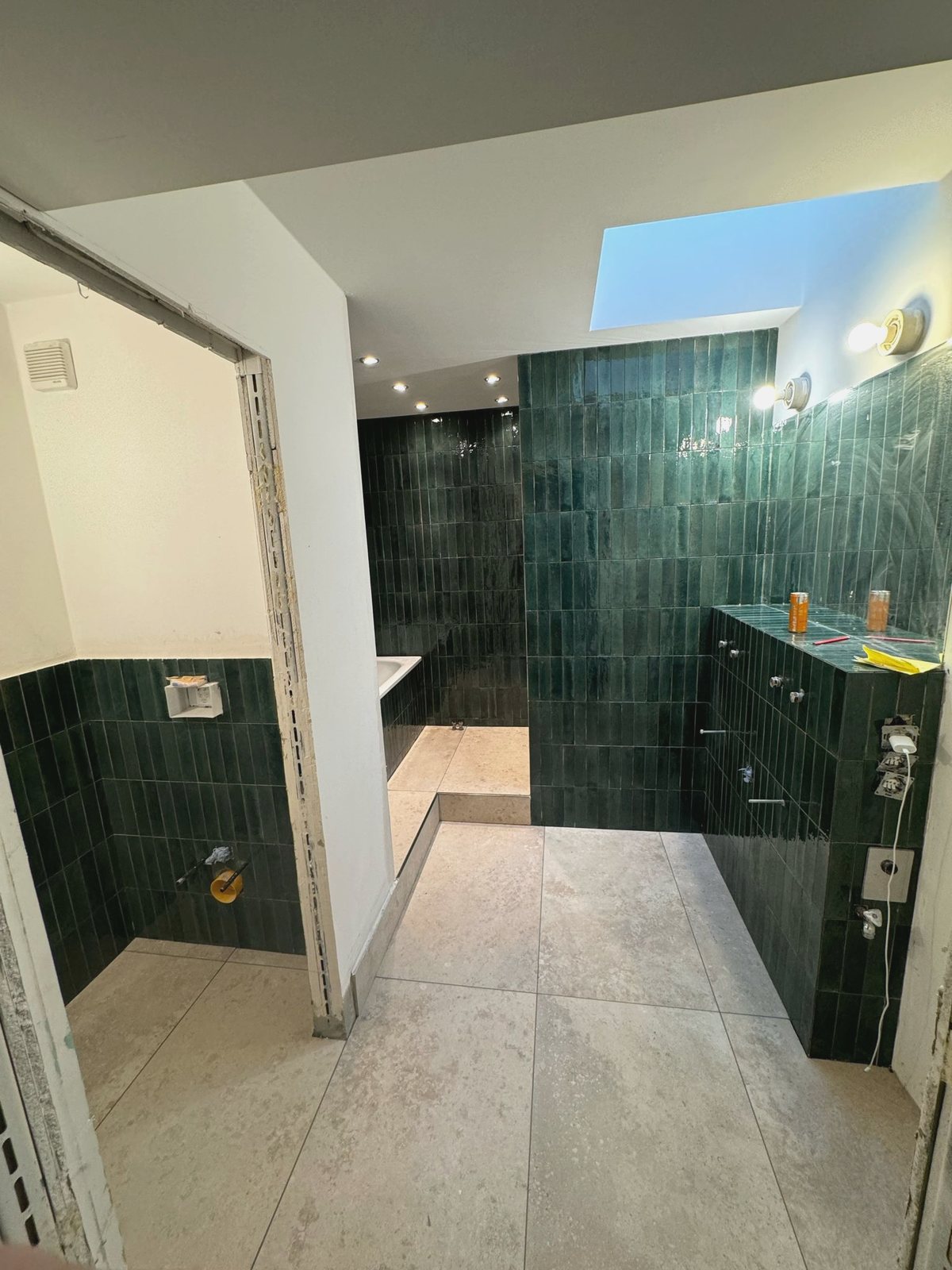 Fertig gefliestes Badezimmer mit grünen Wandfliesen, bodengleicher Dusche und Oberlicht