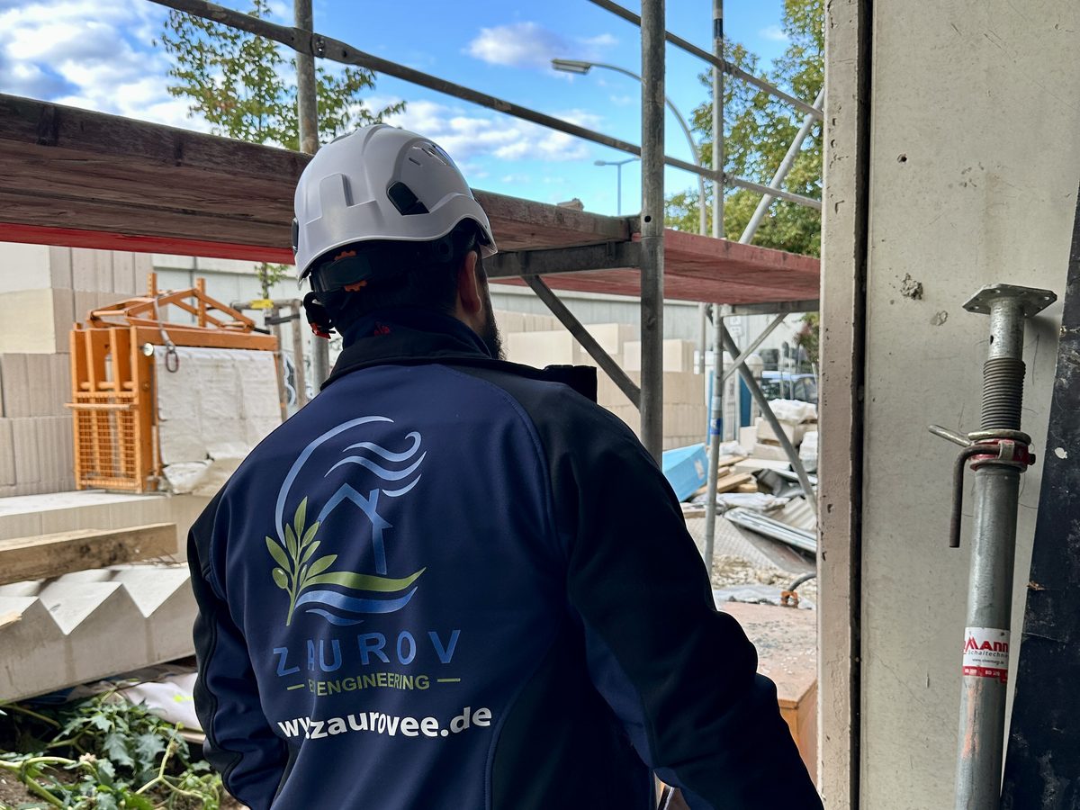 Bauleiter von Zaurov Eco Engineering mit Helm im Rohbau, Firmenjacke mit Logo und Internetadresse