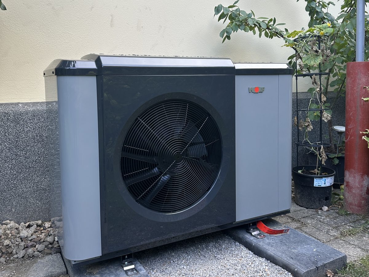 Wolf Monoblock-Wärmepumpe vor einer hellen Hauswand auf zwei Betonplatten mit Kiesbett