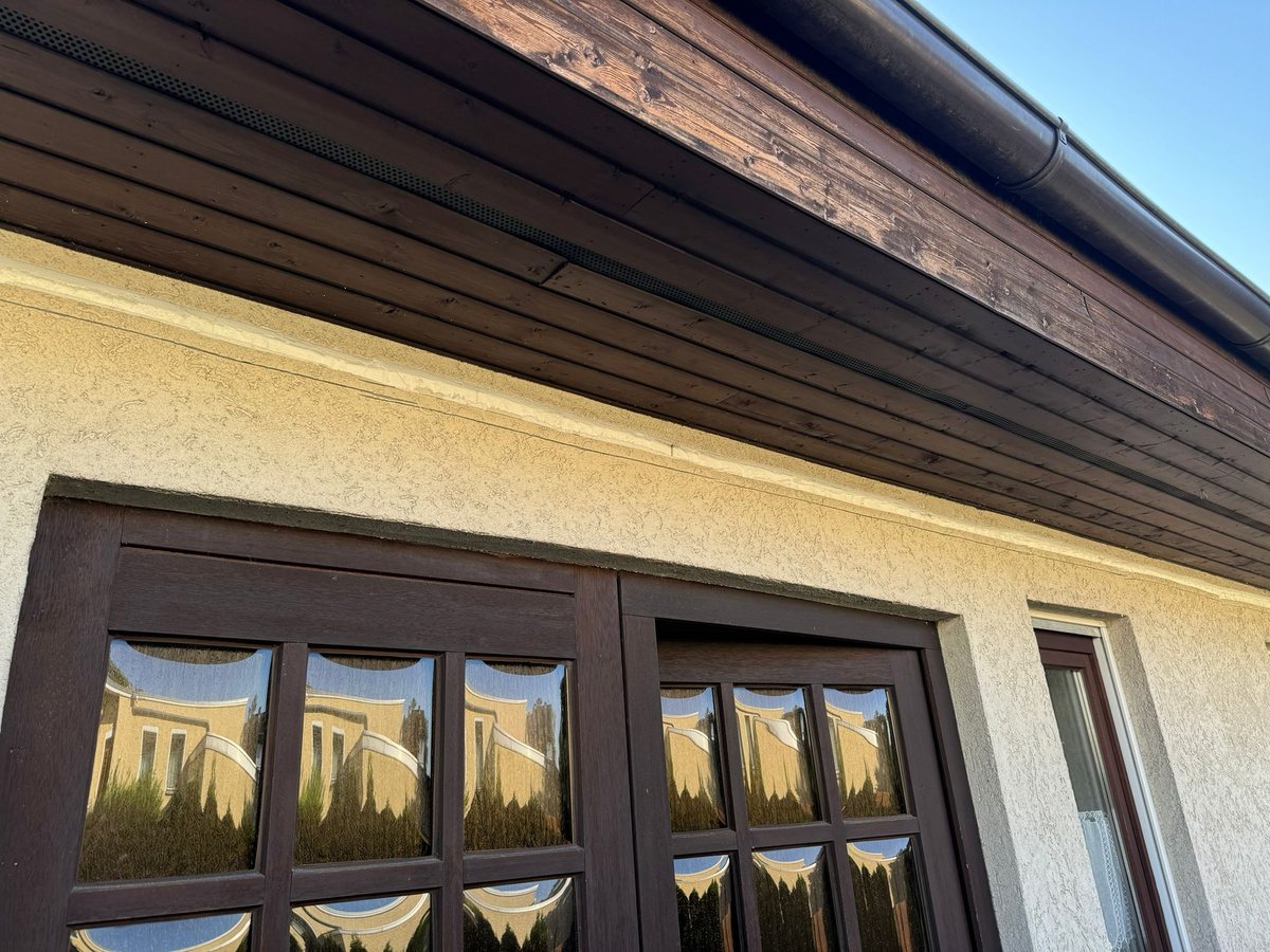 Fenstergruppe mit Holzverkleidung am Dachüberstand, darüber die Leitungsführung der Lüftungsanlage