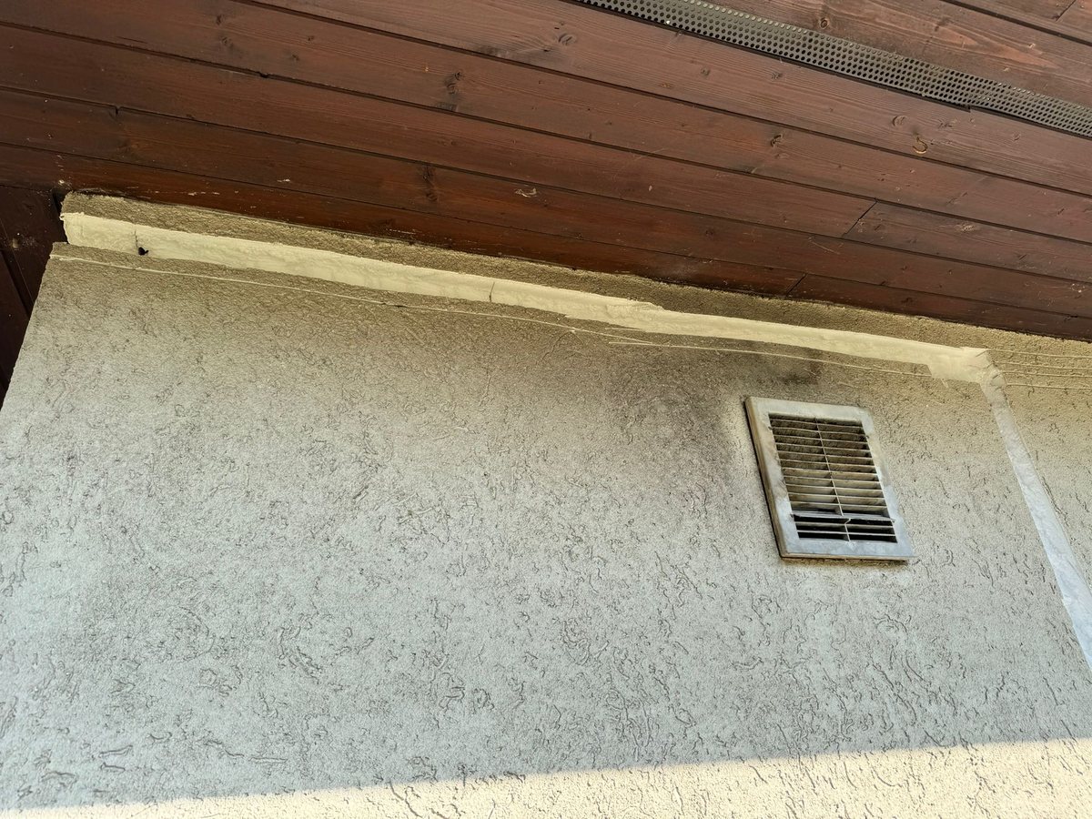 Eckiges Lamellengitter einer Lüftungsöffnung unter dem Dachüberstand einer Putzfassade