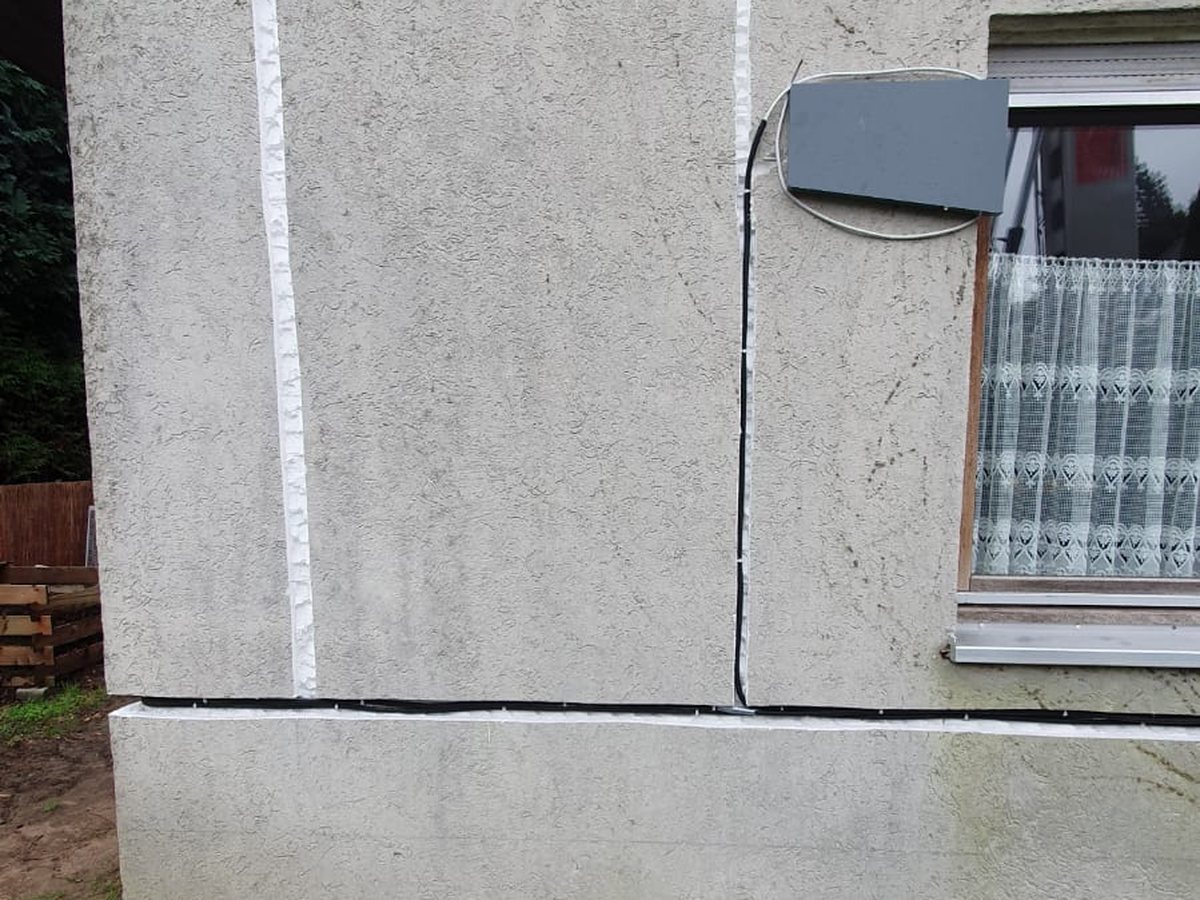 Außenhaube eines dezentralen Lüftungsgeräts neben einem Fenster, die Zuleitung ist um die Hausecke geführt