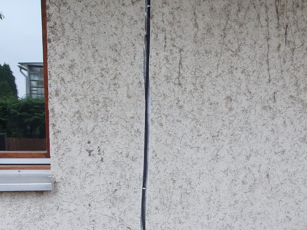 Senkrecht verlegte Stromzuleitung mit Anschlussdose an einer Putzfassade