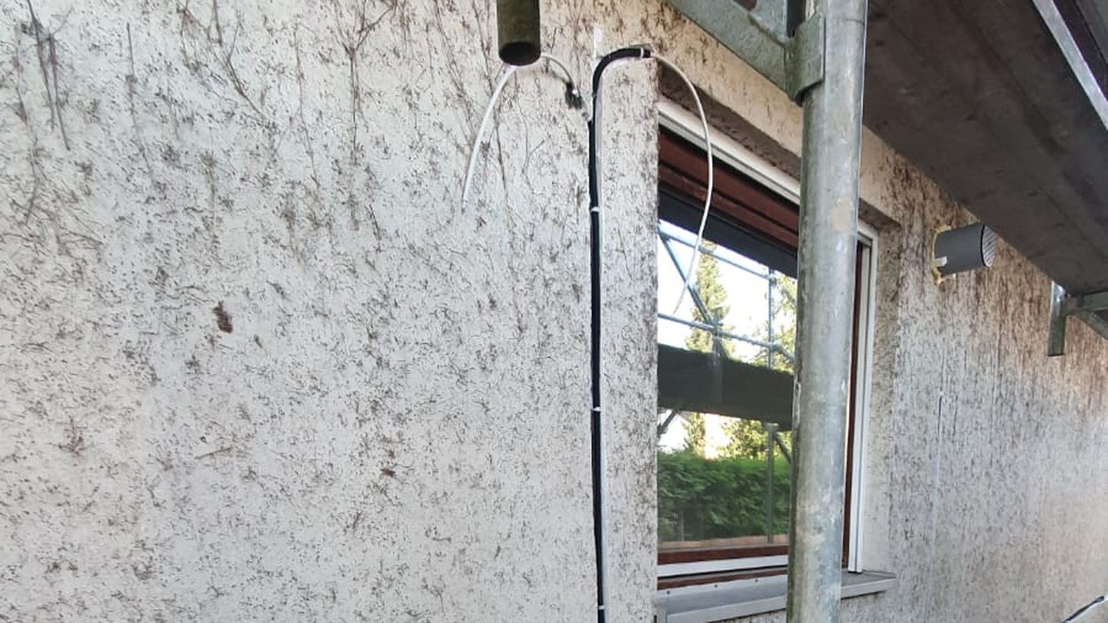 Fassade mit Gerüst: Leitungsführung der Lüftungsgeräte um das Fenster, Außenhaube und Wanddurchführung
