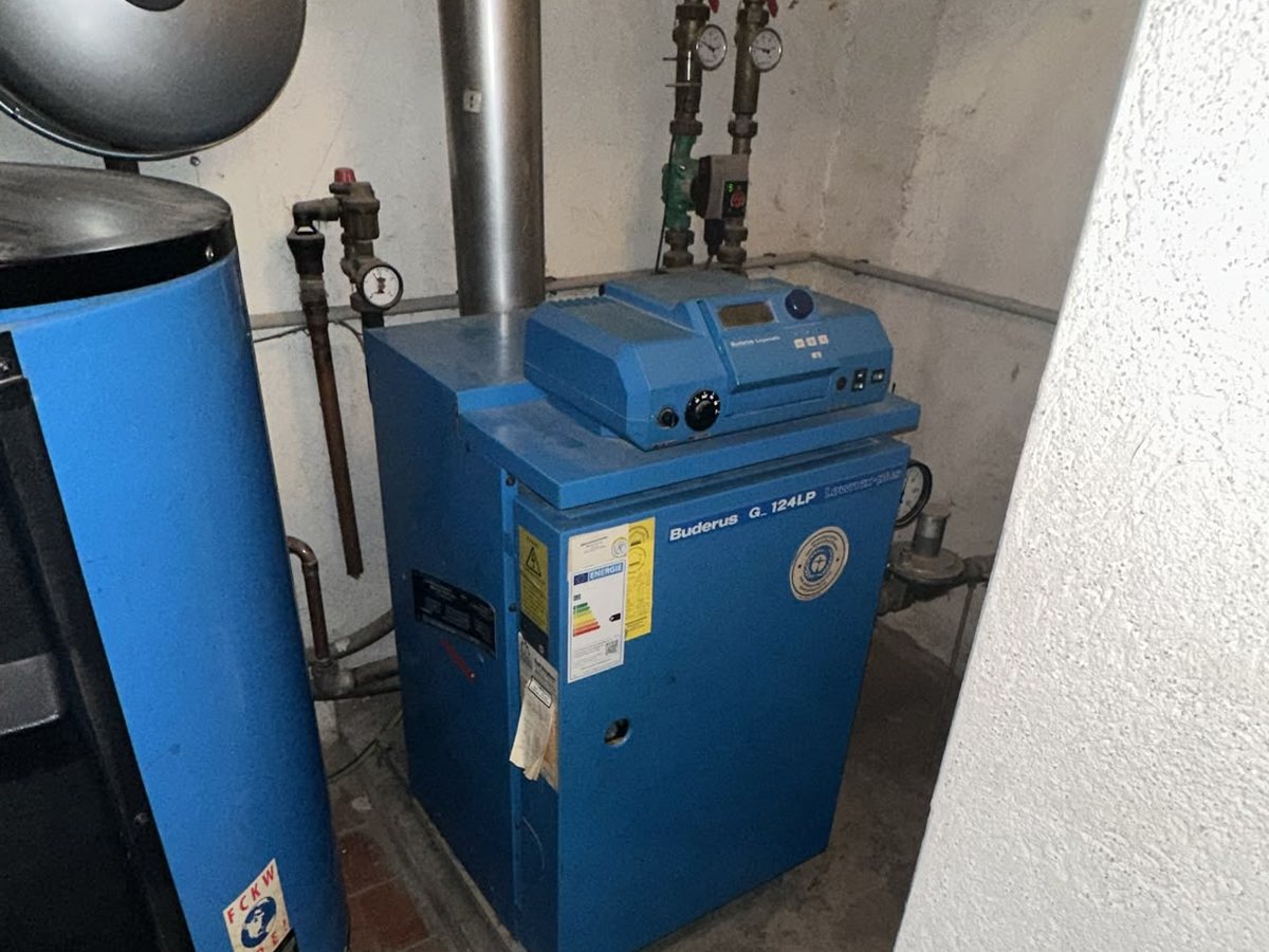 Blauer Buderus-Gaskessel mit Speicher im gefliesten Heizungsraum vor dem Austausch